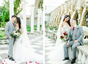 Outdoor Bride and Groom Portrait in Fairy Tale Garden with Columns and Waterfalls | Mermaid Fitted Lace Sweetheart Wedding Gown with Tulle Skirt and Sheer Illusion Panels with Long Cathedral Veil from Tampa Dress Shop Isabel Oneil Bridal Collection | Deep Red Burgundy and Blush Pink Rose Bouquet | Groom Wearing Classic Silver Grey Suit with Burgundy Neck Tie | Kapok Special Events