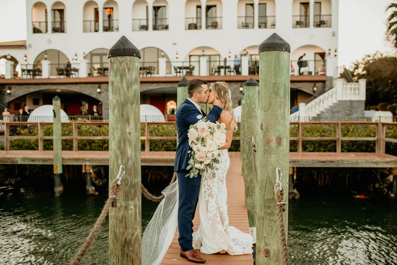 Romantic Intimate Bride and Groom on Waterfront Dock Kissing, Bride Holding Lush White, Ivory and Blush Pink Roses and Eucalyptus Floral Bouquet | St. Pete Boutique Hotel Wedding Venue Hotel Zamora