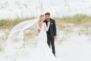 Romantic, Classic Bride in Low V Open Back with Lace Long Sleeves Wedding Dress and Veil Blowing in Wind from Tampa Bay Dress Shop Truly Forever Bridal, Groom in All Black Suit and Blush Pink Bowtie | Styled Shoot