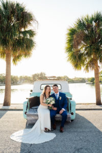 Tampa Bay Bride and Groom On Blue Vintage Rental Truck Outside of Lakefront Wedding Ceremony under Tall Tropical Palm Trees, Bride Holding Modern Bridal Bouquet with Light Ivory and White Florals, Groom in Blue Men's Warehouse Tuxedo with Light Blue Tie | St. Petersburg Women's Club | Florida Day of Wedding Coordinator and Planner Special Moments Event Planning | Grind & Press Photography