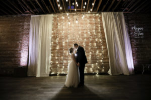 Modern, Simplistic Indoor Tampa Bay Wedding Ceremony, Downtown St. Petersburg Bride and Groom Exchange Vows With Exposed Brick Walls and Romantic String Lighting in Backdrop, White Draping, and Light Gobo of Custom Monogram | Florida Historic Wedding Venue NOVA 535 | St. Petersburg Wedding Photographer Lifelong Photography Studios