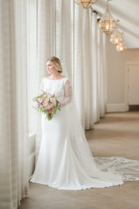 St. Pete Bride in High Scoop Neckline Wedding Dress with Romantic Lace Long Sleeves, Low V Open Back with Buttons Holding Pastel Color Bridal Bouquet with Peach, Pink and Ivory Roses, Greenery, and Lilac Florals | Tampa Bay Wedding Dress Shop Truly Forever Bridal | Don Cesar Styled Shoot