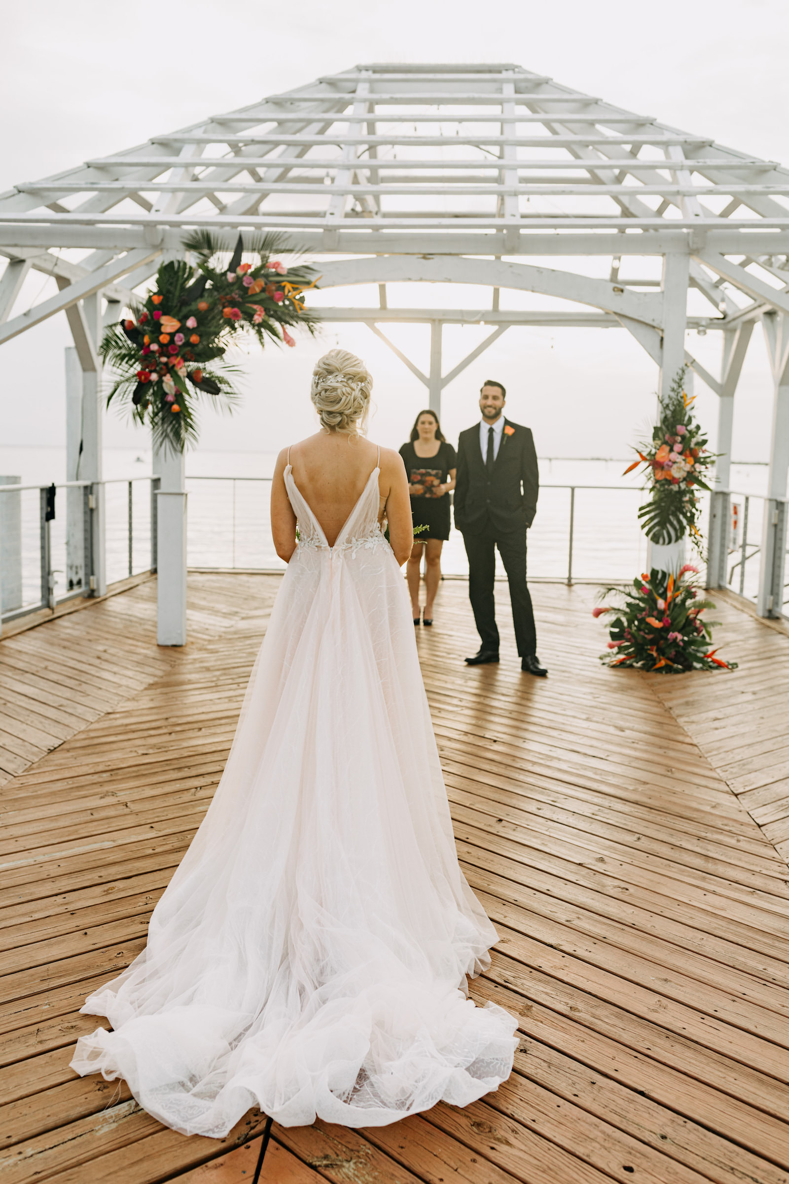 Bride Wearing Romantic Flowy Boho Wedding Dress, Open V Back, Groom and Officiant on Waterfront Pier, Tropical Styled Shoot | Tampa Bay Wedding Venue The Godfrey | Wedding Planner Elope Tampa Bay | Wedding Dress Nikki's Glitz and Glam | Wedding Florist Brides N Blooms | Amber McWhorter Photography