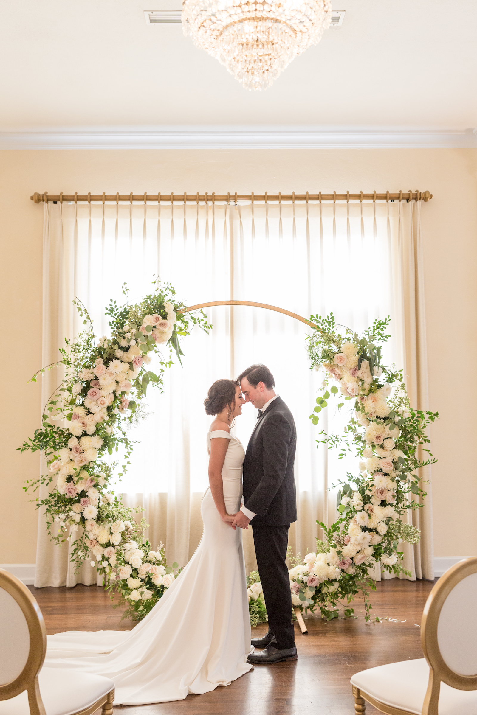 Classic and timeless bride and groom holding hands in front of lush white, blush pink roses floral arrangement on circular arch, eucalyptus and greenery | Tampa Bay wedding planner and designer Elegant Affairs by Design | Kate Ryan Event Rentals | Adore Bridal Hair and Makeup