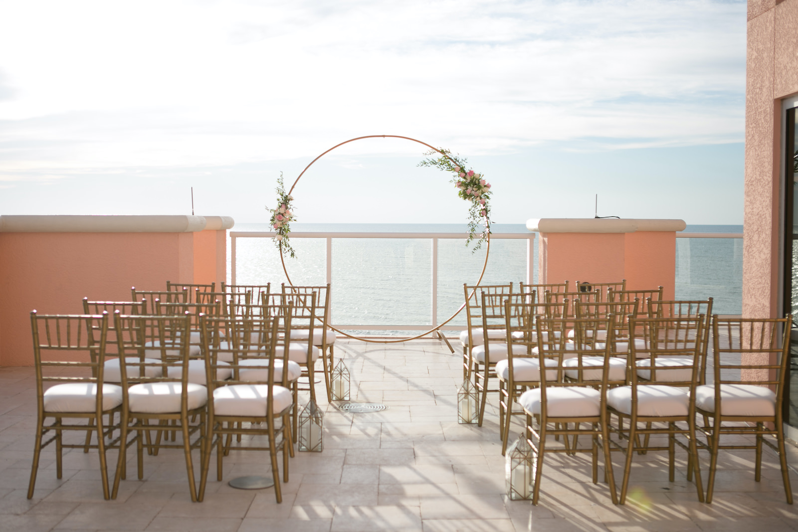 Elegant Modern Wedding Ceremony Decor, Circular Gold Arch with Floral Arrangements, Gold Chiavari Chairs and Lanterns Lining Aisle | Waterfront Hotel Balcony Wedding Venue Hyatt Regency Clearwater Beach | Tampa Bay Wedding Planner Coastal Coordinating | Wedding Photographer Carrie Wildes | Wedding Rentals Outside the Box