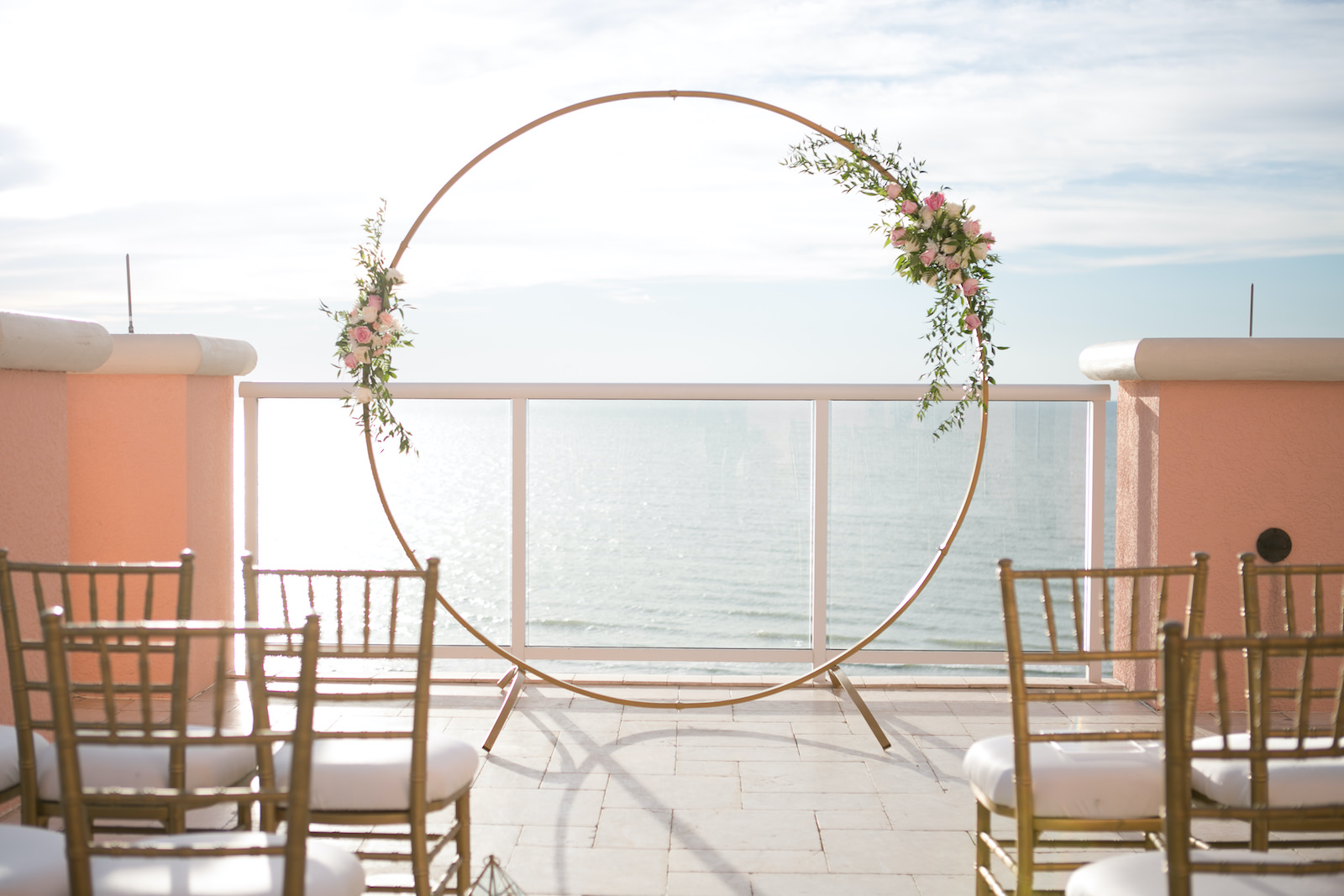 Elegant Modern Wedding Ceremony Decor, Circular Gold Arch with Floral Arrangements, Gold Chiavari Chairs and Lanterns Lining Aisle | Waterfront Hotel Balcony Wedding Venue Hyatt Regency Clearwater Beach | Tampa Bay Wedding Planner Coastal Coordinating | Wedding Photographer Carrie Wildes | Wedding Rentals Outside the Box | Wedding Florist Bride N Blooms