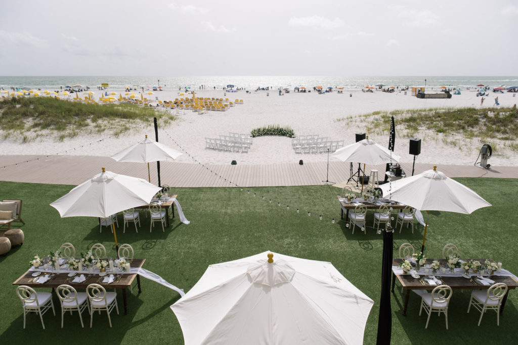Clearwater beach waterfront wedding reception setup, wooden feasting tables and umbrellas | Wedding Venue Sandpearl Resort | Tampa Bay Wedding Planner Parties A'la Carte | Wedding Rentals Kate Ryan Event Rentals | Sandpearl Resort