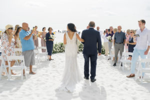 Romantic Classic bride walking down the aisle on sandy beach with dad in open v back lace wedding dress | Tampa Bay boutique bridal shop Isabel O'Neil | Clearwater Beach wedding venue Sandpearl Resort