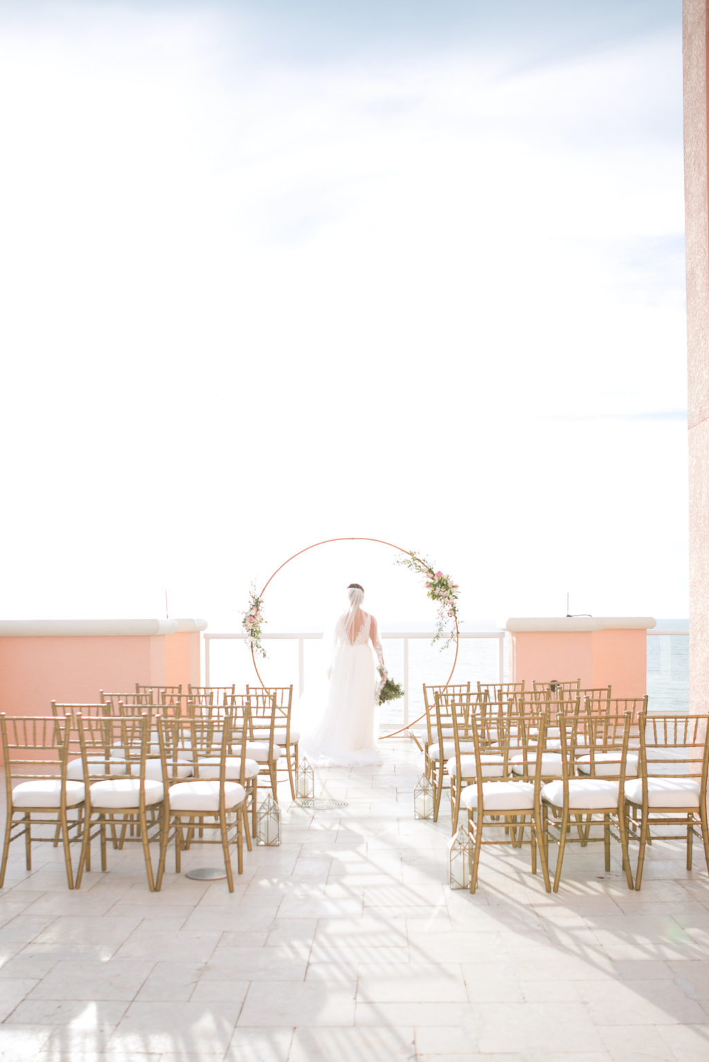 Elegant Modern Wedding Ceremony Decor, Circular Gold Arch with Floral Arrangements, Gold Chiavari Chairs and Lanterns Lining Aisle | Waterfront Hotel Balcony Wedding Venue Hyatt Regency Clearwater Beach | Tampa Bay Wedding Planner Coastal Coordinating | Wedding Photographer Carrie Wildes | Wedding Rentals Outside the Box | Wedding Florist Brides N Blooms Designs