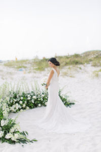 Clearwater Beach Bride on sand wearing lace open v back wedding dress, half circle floral arrangement of tall white flowers and greenery | Tampa Bay wedding planner Parties A'la Carte | Wedding dress shop Isabel O'Neil Bridal