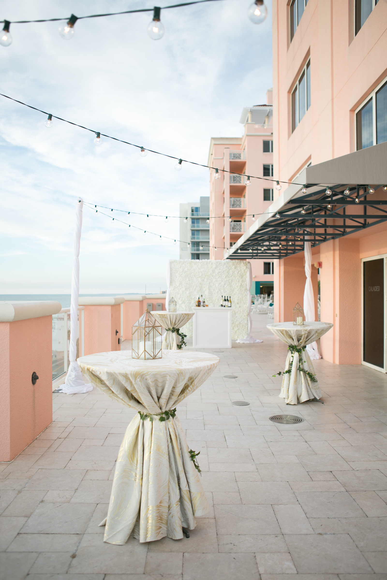 Modern Elegant Hotel Balcony Waterfront Wedding Venue Hyatt Regency Clearwater Beach, Cocktail Hour Wedding Decor, Tall Round Tables with Neutral Linens, Greenery and Lantern | Tampa Bay Wedding Planner Coastal Coordinating | Wedding Rentals Outside the Box | Wedding Photographer Carrie Wildes | Wedding Planner Coastal Coordinating