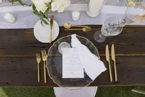 Garden-style wedding reception decor, gold rimmed and clear chargers, gold flatware, custom white and blue font menu, white linen table runner | Tampa Bay Wedding Planner Parties A'la Carte | Kate Ryan Event Rentals
