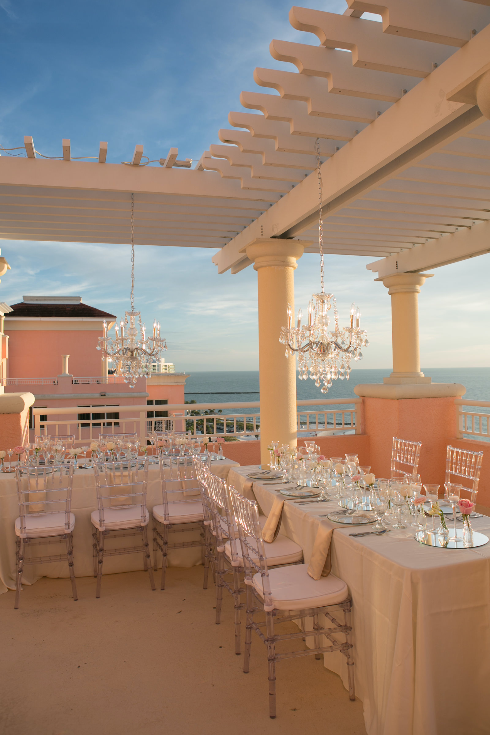 Elegant Modern Wedding Reception Decor on Rooftop Balcony of Waterfront Wedding Venue Hyatt Regency Clearwater Beach, Long Tables with Acrylic Chiavari Chairs, Hanging Crystal Chandeliers | Tampa Bay Wedding Photographer Carrie Wildes | Wedding Planner Coastal Coordinating | Wedding Rentals Outside the Box