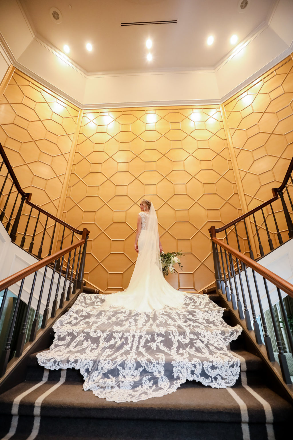 Bride in Romantic Lace and Illusion Overlay and Long Train, Full Length Veil Holding White and Greenery Floral Bouquet on Staircase | Wedding Venue The Tampa Club | Wedding Dress Truly Forever Bridal | Wedding Photographer Lifelong Photography Studio | Styled Shoot