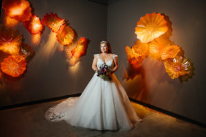 Halloween Bride Wearing Lace and Tulle Cap Sleeve Ballgown Wedding Dress, Whimsical Artsy Orange Red Glass Flower Light Wall Fixtures at Chihuly Collection | Tampa Bay Wedding Dress Shop Truly Forever Bridal
