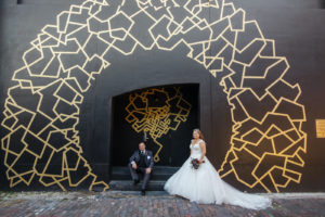 Halloween Bride and Groom Outside Black Building with Gold Whimsical Painted Geometric Shapes, Bride in Lace and Tulle Capsleeve Ballgown Wedding Dress | Tampa Bay Wedding Dress Shop Truly Forever Bridal