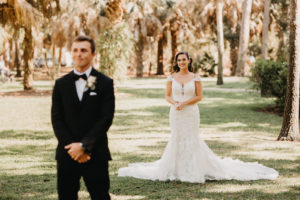 Florida Bride in Romantic Lace, Illusion and Cap Sleeve Maggie Sottero Wedding Dress First Look Photo with Grooms Back to Bride in Black Tuxedo