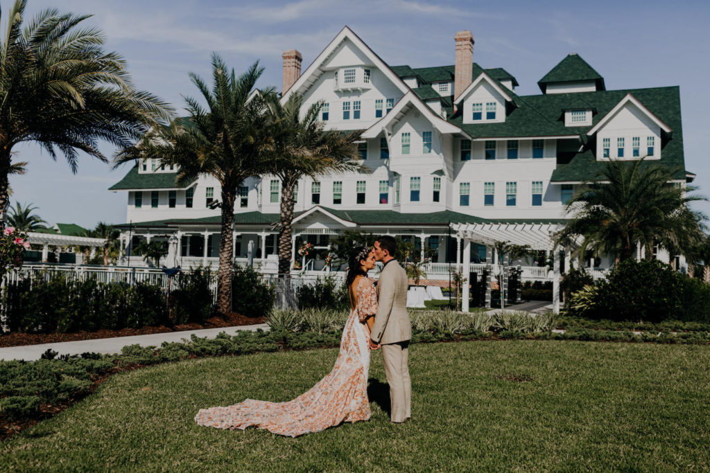 Outdoor Bride and Groom Wedding Portrait at Historic Clearwater Venue Belleview Inn | Boho Gold Bronze Embroidered Overlay Wedding Dress Bridal Gown with Illusion Sleeves and Train | Groom in Grey Khaki Linen Suit