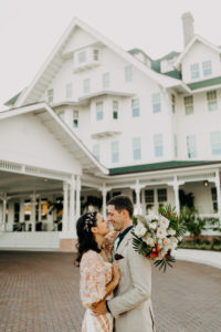 Outdoor Bride and Groom Wedding Portrait at Historic Clearwater Venue Belleview Inn | Boho Gold Bronze Embroidered Overlay Wedding Dress Bridal Gown with Illusion Sleeves and Train | Groom in Grey Khaki Linen Suit