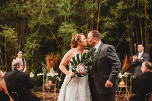 Modern Tropical Inspired Wedding Ceremony in Bamboo Garden, Bride and Groom Kiss at End of Aisle, Bride Wearing Blush By Hayley Paige Delta Wedding Dress, Holding King Protea and Monstera Leaf Minimalist DIY Bridal Bouquet | Downtown St. Pete Historic Wedding Venue NOVA 535