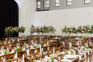 Indoor Tampa Christmas Wedding Reception with Wood Farm Feasting Tables and Tall Gold Centerpieces of Red White and Gold Cafe au Lait Roses and Winter Greenery and Berries | Long Red White and Gold Rose Garland Centerpiece with Winter Greenery