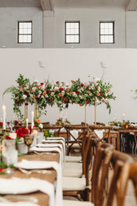 Indoor Tampa Christmas Wedding Reception with Wood Farm Feasting Tables and Tall Gold Centerpieces of Red White and Gold Cafe au Lait Roses and Winter Greenery and Berries