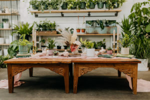 Boho Styled Shoot Decor | Vintage Wooden Tables with Pink Runner, Unique Floral Bouquet with Pampas Grass, Dried Flowers, Pink Anthurium, Ivory Roses, Greenery Plants, Gold Candlesticks | Unique St. Pete Wedding Venue Wild Roots Nursery | Amber McWhorter Photography | Wedding Planner Elope Tampa Bay