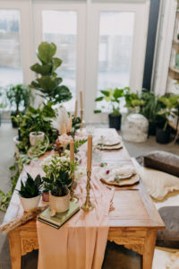 Boho Neutral Styled Shoot Decor | Vintage Wooden Table with Gold Candlesticks, Wooden Chargers, Pink Linen Table Runner, Greenery Plants | Wedding Planner Elope Tampa Bay | Unique St. Pete Wedding Venue Wild Roots | Amber McWhorter Photography | Wooden Chargers and Rose Gold Flatware Rentals Kate Ryan Event Rentals