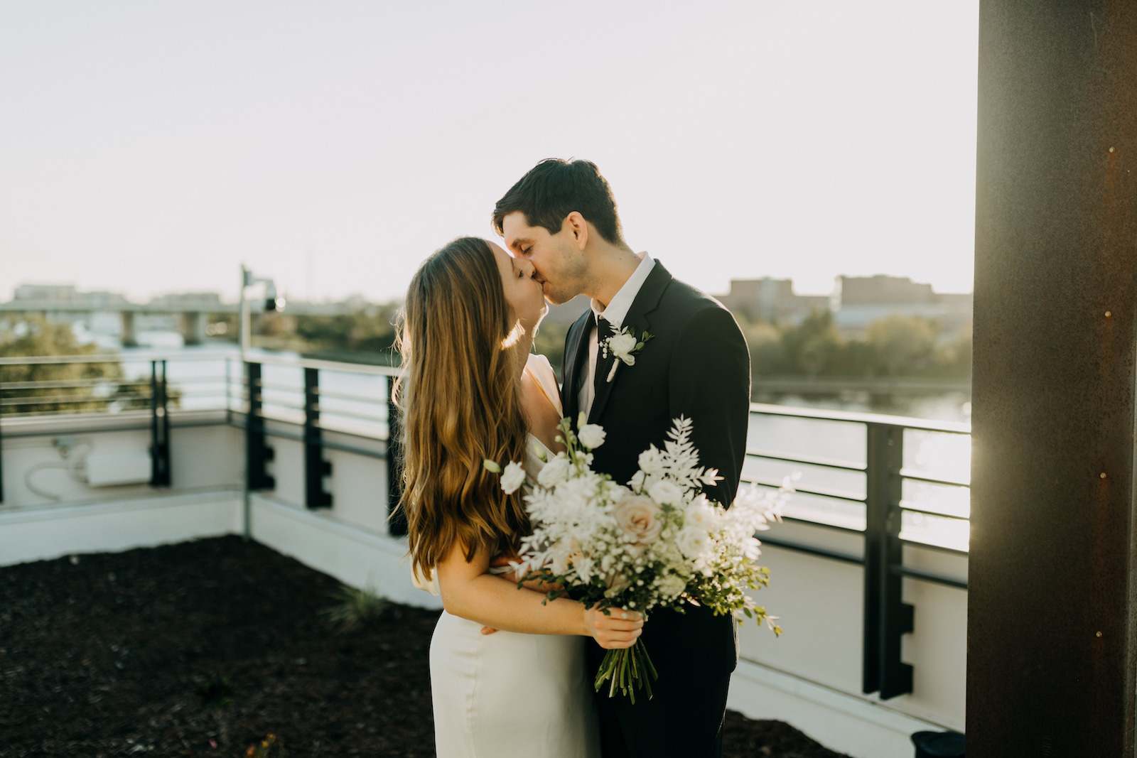 Modern Industrial Bride and Groom Exchanging Kiss Holding All White Neutral Floral Bouquet | Tampa Bay Wedding Planner Elope Tampa Bay | Wedding Venue Rooftop 220 | Wedding Photographer Amber McWhorter