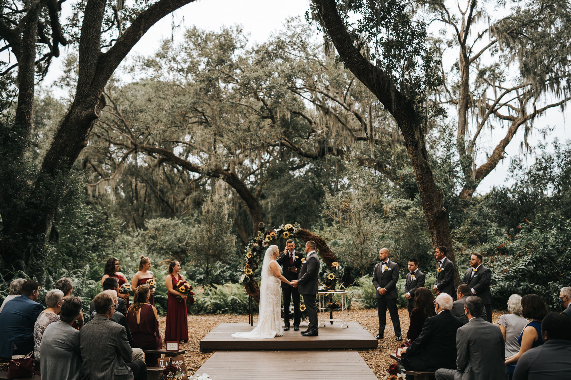 Rustic Dover Burgundy and Yellow Sunflower Outdoor Wedding Ceremony with Wood Benches and Round Grapevine Branch Arch | Long Chiffon Burgundy Bridesmaid Dresses | Groom and Groomsmen in Classic Charcoal Grey Gray Suit Tux with Sunflower Boutonniere