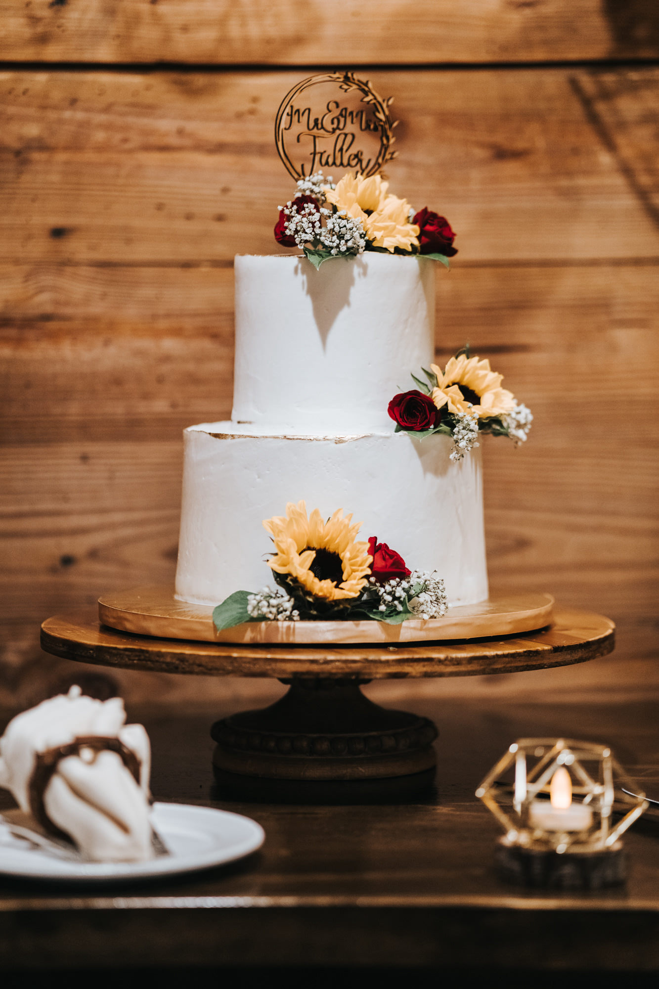 Two Tier Simple Smooth Buttercream Wedding Cake with Yellow Sunflowers and Red Roses and Baby's Breath topped with Die Cut Wood Name Cake Topper