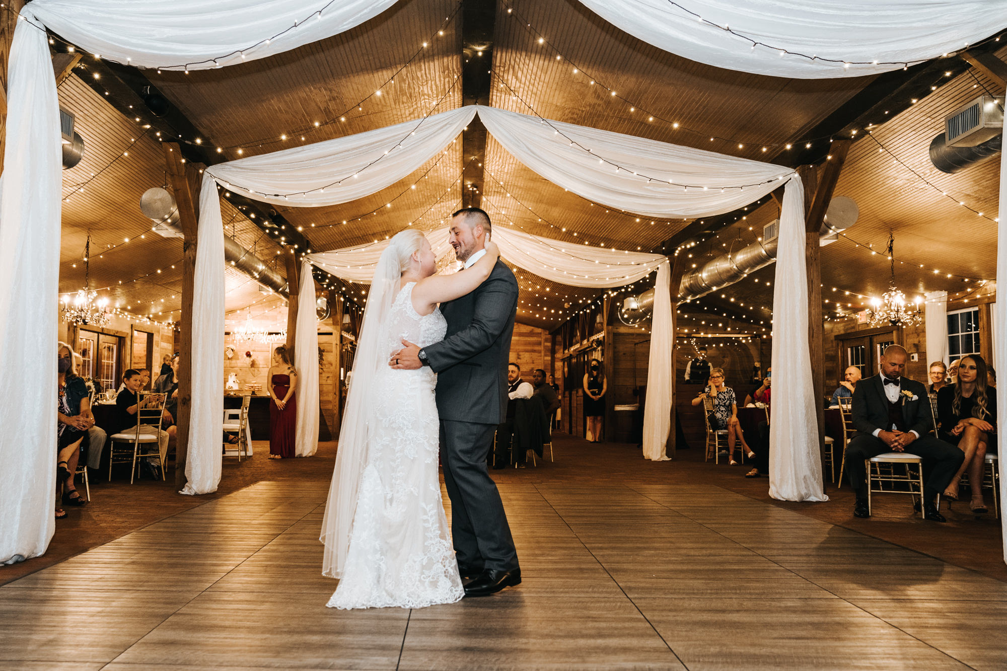 Bride and Groom First Dance during Rustic Dover Wedding Barn Reception with String Lights and Ceiling Draping