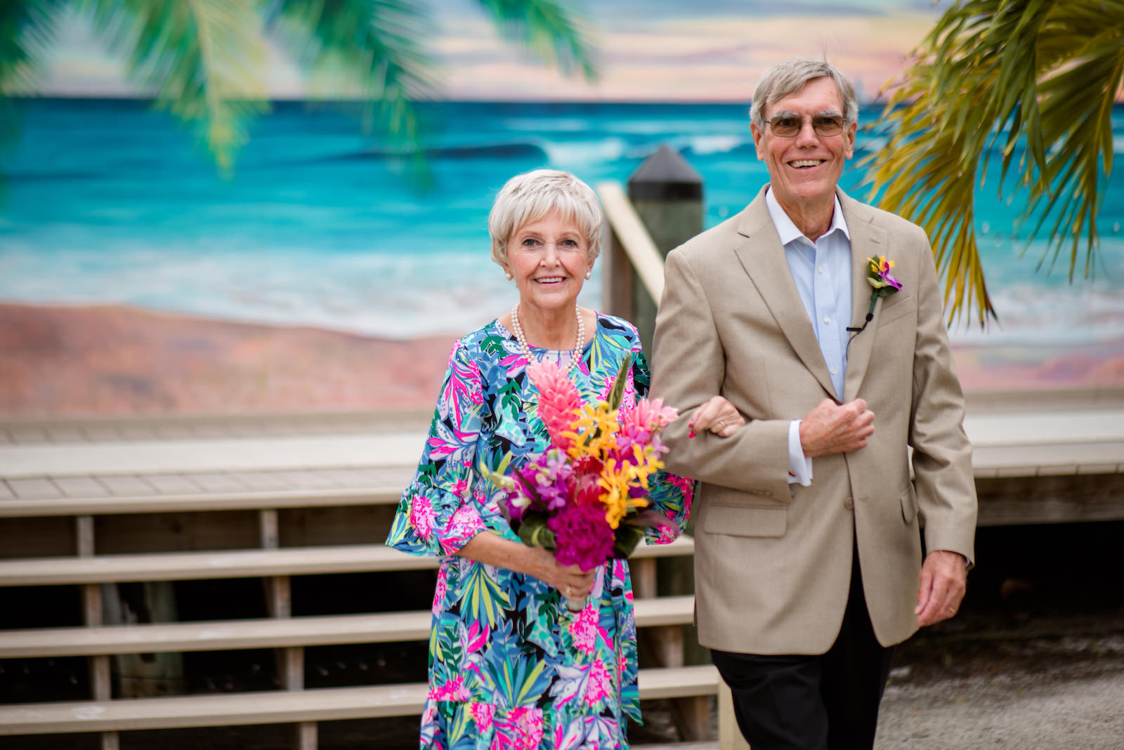 Tropical Inspired Florida Vow Renewal, Husband and Wife Walk Down Aisle At Milestone Anniversary Vow Renewal, Bride Wearing Lilly Pulitzer Dress, Carrying Vibrant Exotic Floral Bouquet with Pink, Purple and Yellow Flowers | Tampa Bay Vow Renewal and Microwedding Planners Perfecting The Plan | St. Petersburg Wedding Venue Isla Del Sol