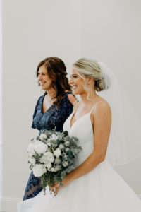 Classic Bride in V Neckline Horsehair Trim Full Ruffle Skirt Wedding Dress Walking Down the Wedding Ceremony Aisle with Mom Holding White and Greenery Floral Bouquet | Tampa Bay Wedding Photographer Amber McWhorter Photography | Wedding Hair and Makeup Femme Akoi Beauty Studio