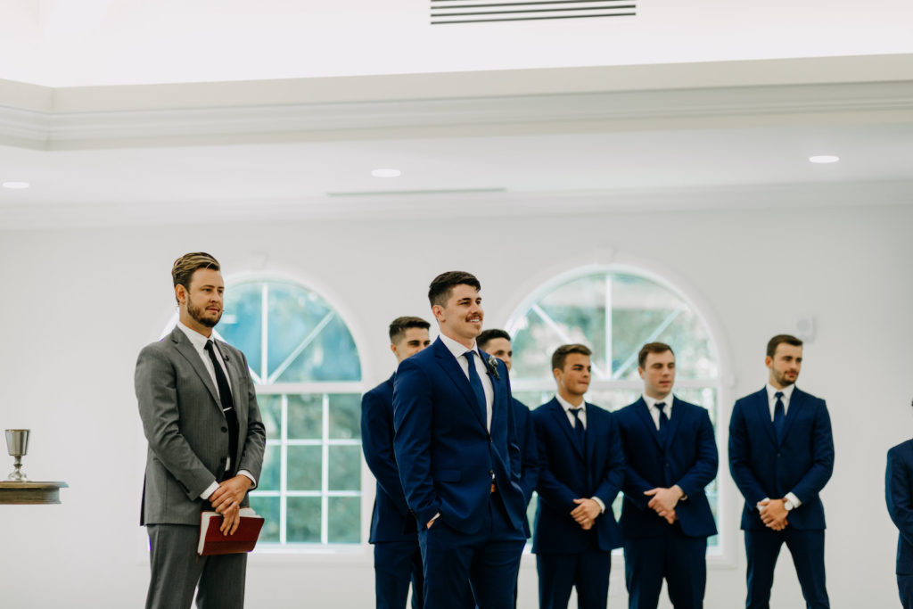 Groom in Navy Blue Suit Reaction to Bride Walking Down the Wedding Ceremony Aisle | Tampa Bay Wedding Photographer Amber McWhorter Photography | Traditional Safety Harbor Wedding Venue Harborside Chapel