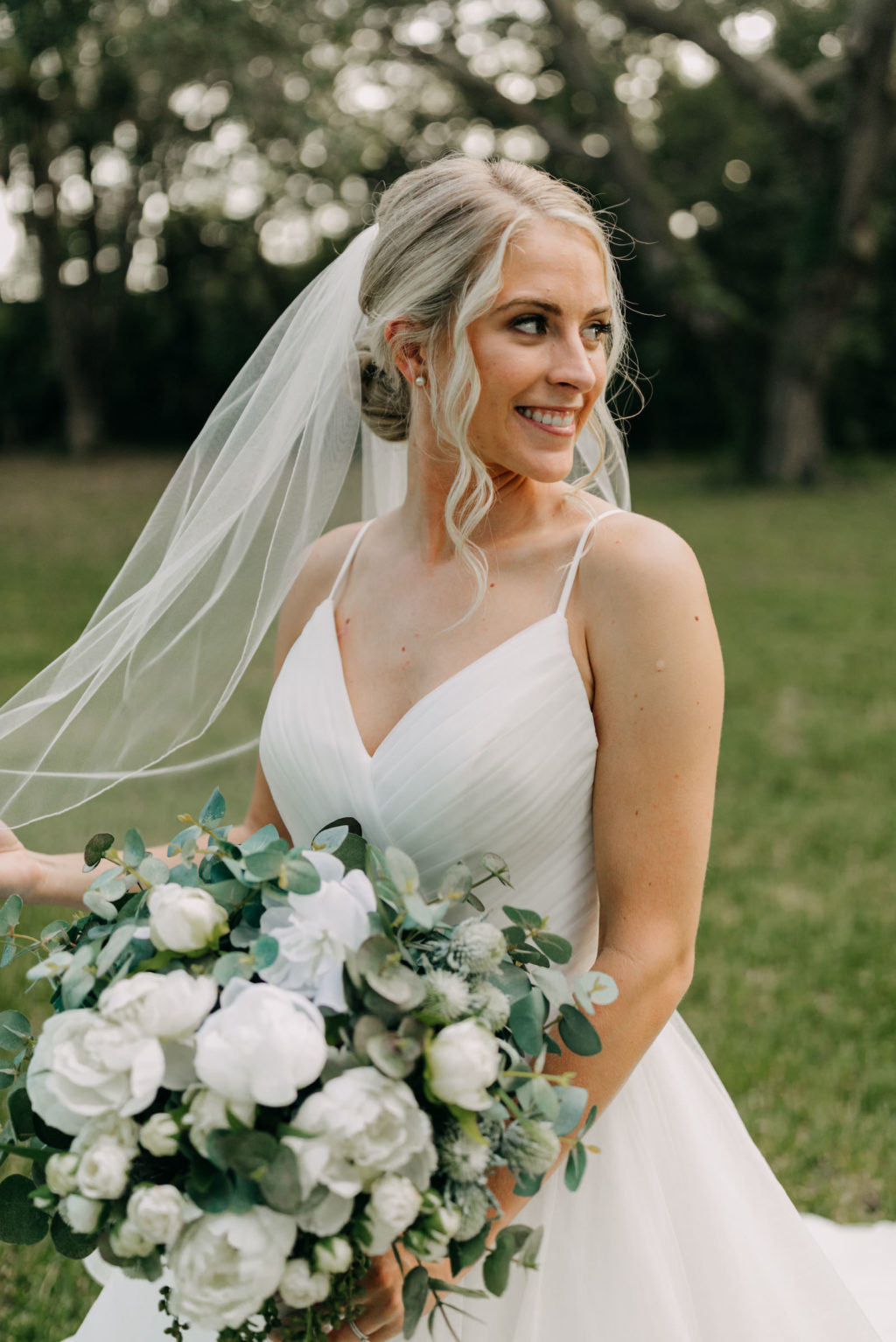 Classic Bride with Neutral Makeup and Hair in Bun and Veil in V Neckline Wedding Dress Holding White Floral and Greenery Eucalyptus Bouquet | Tampa Bay Wedding Photographer Amber McWhorter Photography | Wedding Hair and Makeup Femme Akoi Beauty Studio