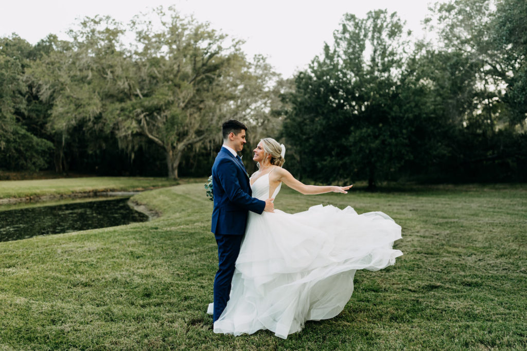Classic Bride with Hair in Bun and Veil in V Neckline Wedding Dress Holding Eucalyptus Greenery and White Floral Bouquet with Groom in Blue Suit | Tampa Bay Wedding Photographer Amber McWhorter Photography | Wedding Hair and Makeup Femme Akoi Beauty Studio