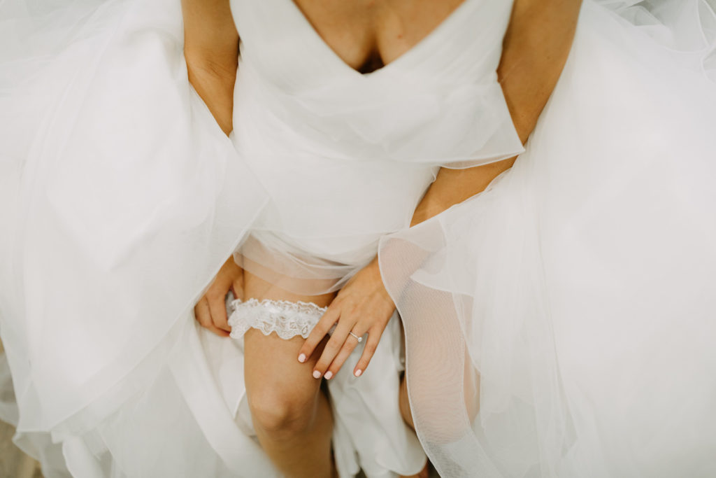 Florida Bride Wedding Ready Putting On Lace Garter Wearing Horsehair Trim Ruffle Skirt V Neckline Wedding Dress | Tampa Bay Wedding Photographer Amber McWhorter Photography