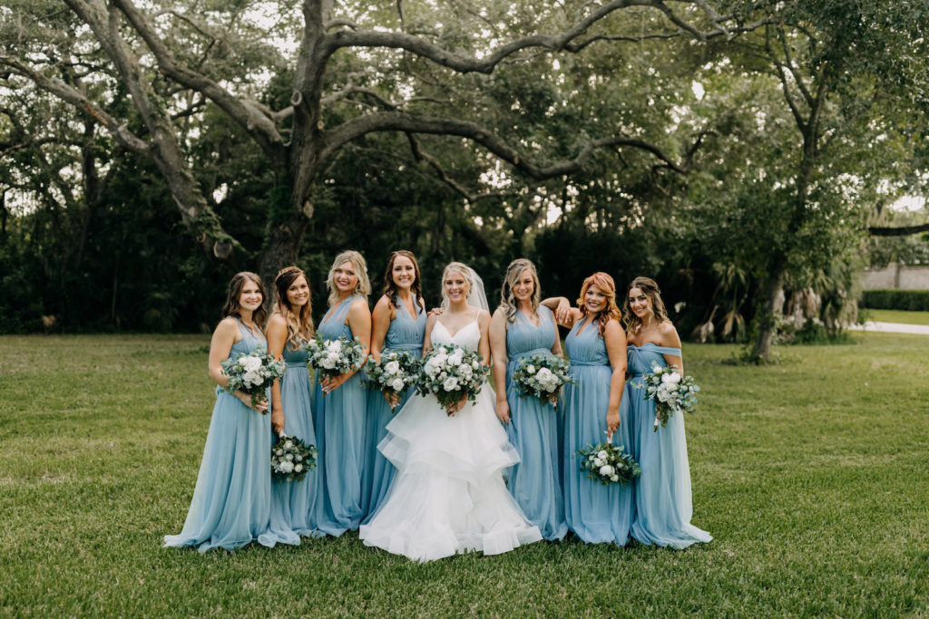 Classic Bride in Full Skirt V Neckline Wedding Dress with Bridesmaids in Matching Dusty Blue Dresses Holding White and Greenery Floral Bouquets| Tampa Bay Wedding Photographer Amber McWhorter Photography | Wedding Hair and Makeup Femme Akoi Beauty Studio