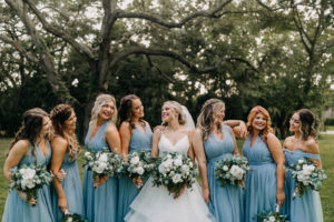 Classic Bride in Full Skirt V Neckline Wedding Dress with Bridesmaids in Matching Dusty Blue Dresses Holding White and Greenery Floral Bouquets| Tampa Bay Wedding Photographer Amber McWhorter Photography | Wedding Hair and Makeup Femme Akoi Beauty Studio
