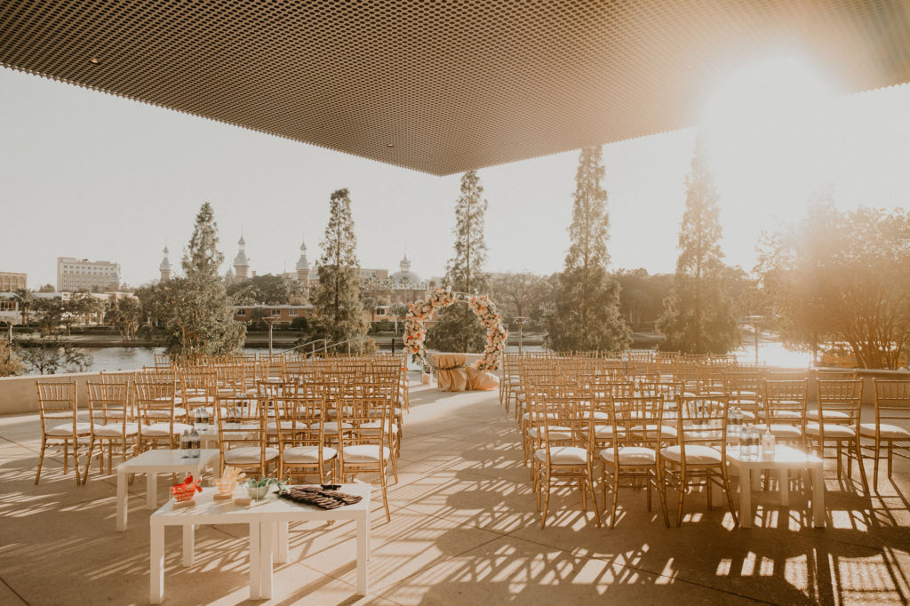 Outdoor Downtown Tampa Waterfront Wedding Ceremony with Gold Chiavari Chairs and Round Arch Floral Arrangement with Peach Salmon Coral Roses White Hydrangea and Eucalyptus Greenery