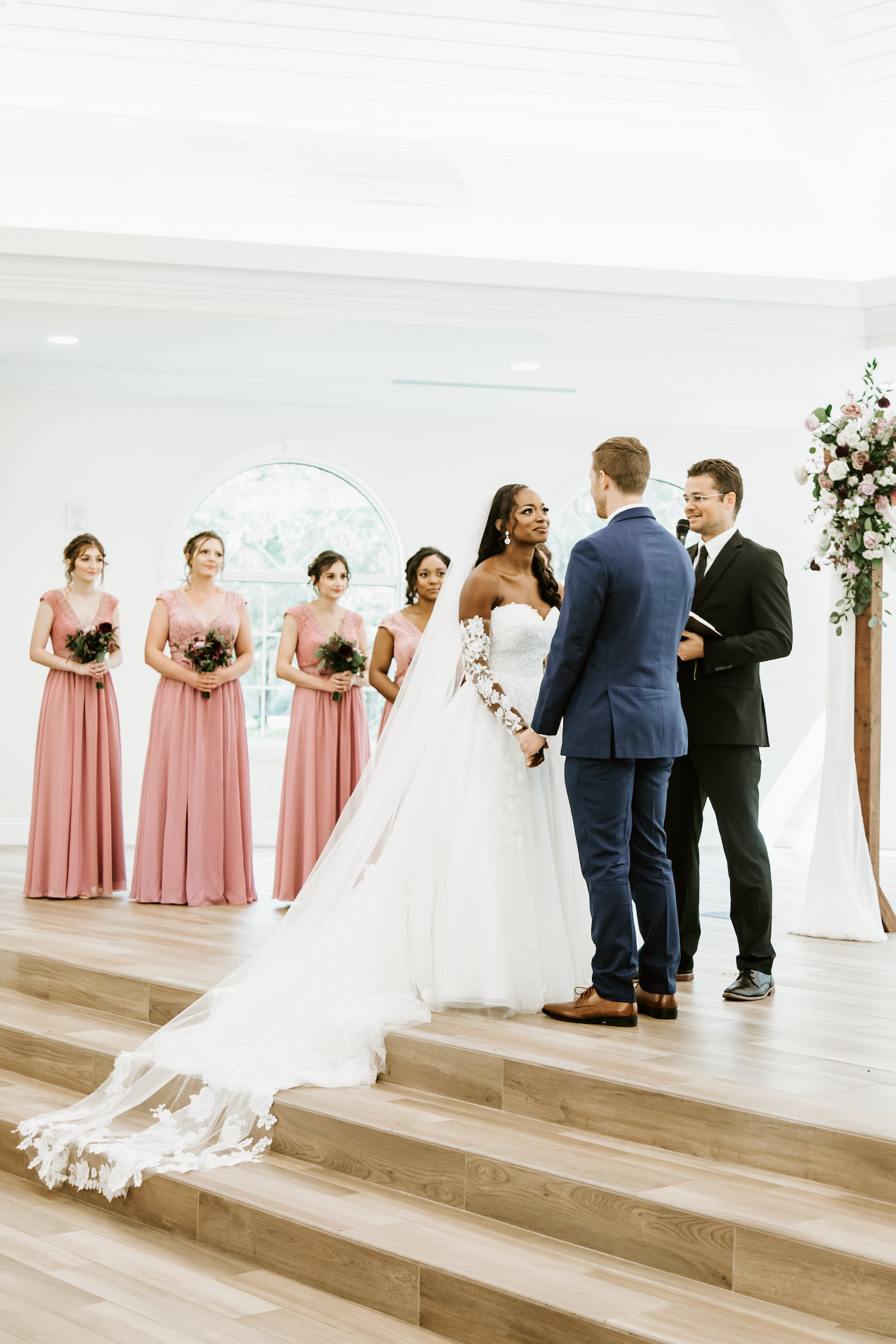 Indoor Church Wedding Ceremony at St. Pete Wedding Venue Harborside Chapel | Blush Pink Dusty Rose Mauve Bridesmaid Dresses | Tulle and Lace Ballgown Wedding Dress with Long Sleeves and Cathedral Length Veil | Groom in Navy Blue Suit