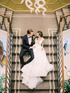 Indoor Bride and Groom Portrait at Downtown Tampa Wedding Venue The Tampa Club Staircase | V Neck Embroidered Illusion Panel Allure Couture Designer Wedding Dress Bridal Gown | Groom in Classic Black Suit Tux with Bow Tie