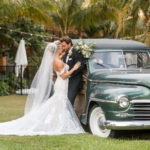 Elegant Sarasota Bride and Groom With Vintage Car at Anna Marie Island Courtyard Wedding | Bride Wearing White Fit and Flare Wedding Dress with Off the Shoulder Lace Sleeves, Holding Lush Ivory Floral Bouquet with Greenery, Groom in Classic Black Tuxedo | Florida Wedding Photographer Lifelong Photography Studio | Tampa Bay Wedding PlannerKelly Kennedy Weddings