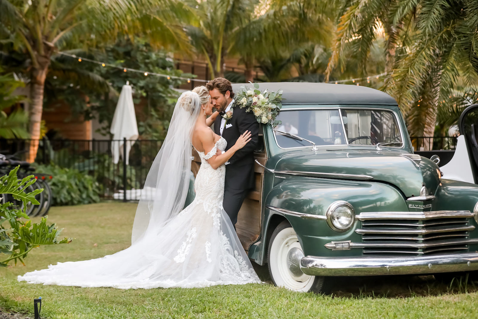 Elegant Sarasota Bride and Groom With Vintage Car at Anna Marie Island Courtyard Wedding | Bride Wearing White Fit and Flare Wedding Dress with Off the Shoulder Lace Sleeves, Holding Lush Ivory Floral Bouquet with Greenery, Groom in Classic Black Tuxedo | Florida Wedding Photographer Lifelong Photography Studio | Tampa Bay Wedding PlannerKelly Kennedy Weddings