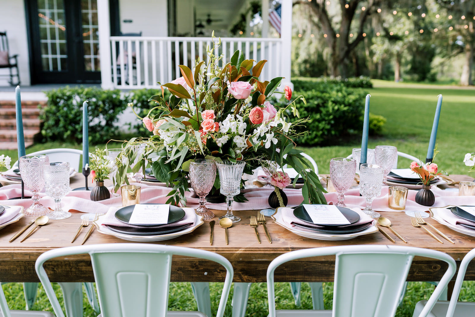 Southern Elegant Inspired Florida Outdoor Wedding Reception, Long Wooden Feasting Table with Dark Blue Place Setting, Gold Flatware, Pink Burlap Linens, Tall Blue Candelabras, Low Floral Centerpiece with Pink Roses, Orange Florals, and Magnolia Leaf Greenery | Tampa Bay Wedding Planner EventFull Weddings | Florida Wedding Linen Rentals Over The Top Linen Rentals