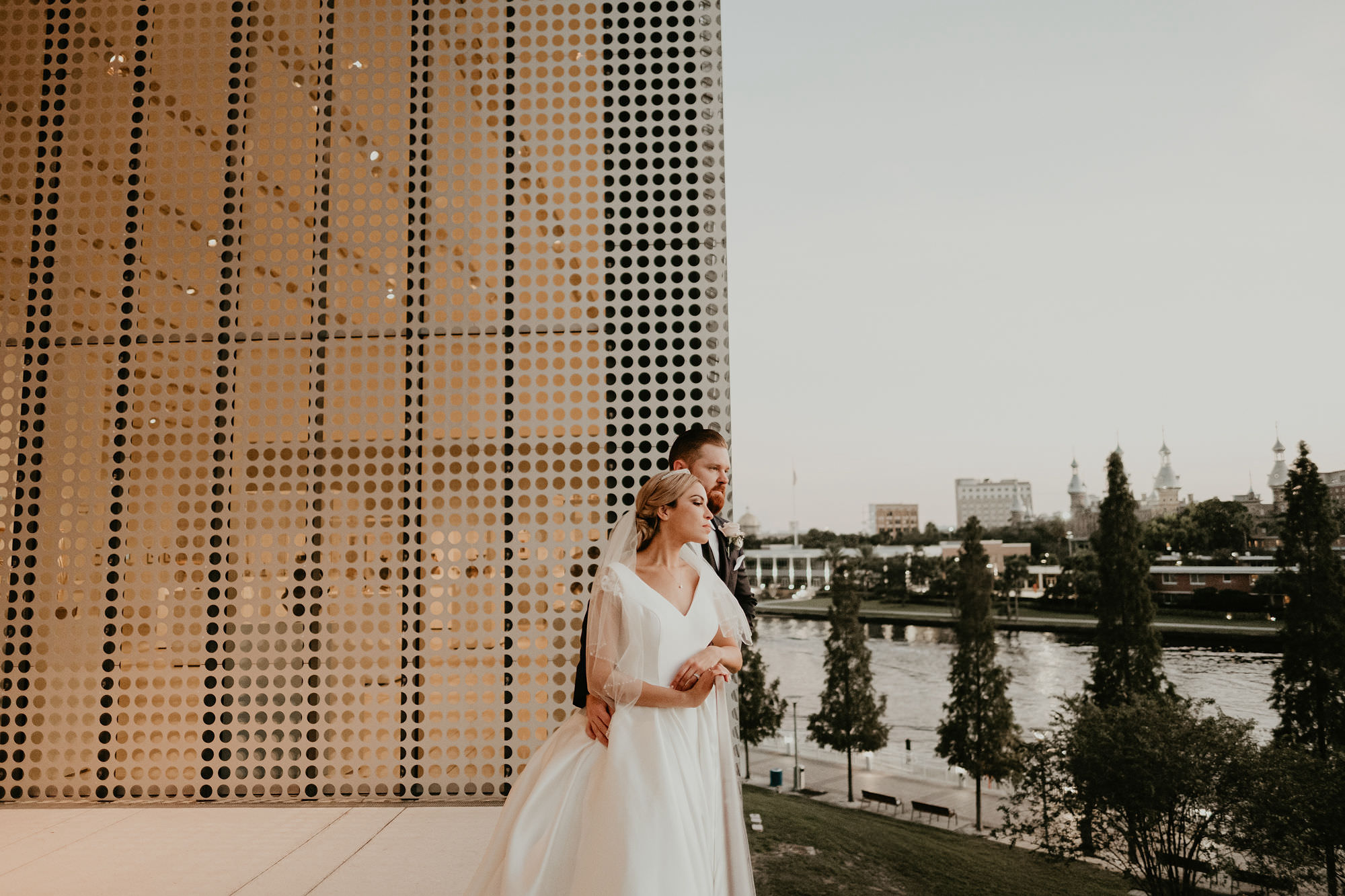 Outdoor Downtown Tampa Waterfront Bride and Groom Portrait at Tampa Museum of Art | V Neck Mikado Satin Ballgown Wedding Dress by Anomalie | Groom Wearing Classic Black Suit Tux
