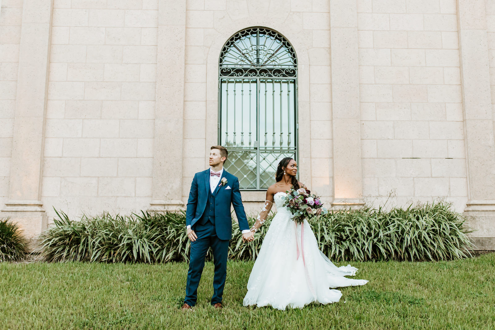 Bride and Groom Outdoor Portrait in Downtown St. Pete | Lace and Tulle Ballgown Bridal Gown Wedding Dress with Illusion Lace Long Sleeves | Navy Groom Suit | Bridal Bouquet with Ivory Pink and Burgundy Maroon Roses with Eucalyptus Greenery and Cascading Pink Velvet Ribbons