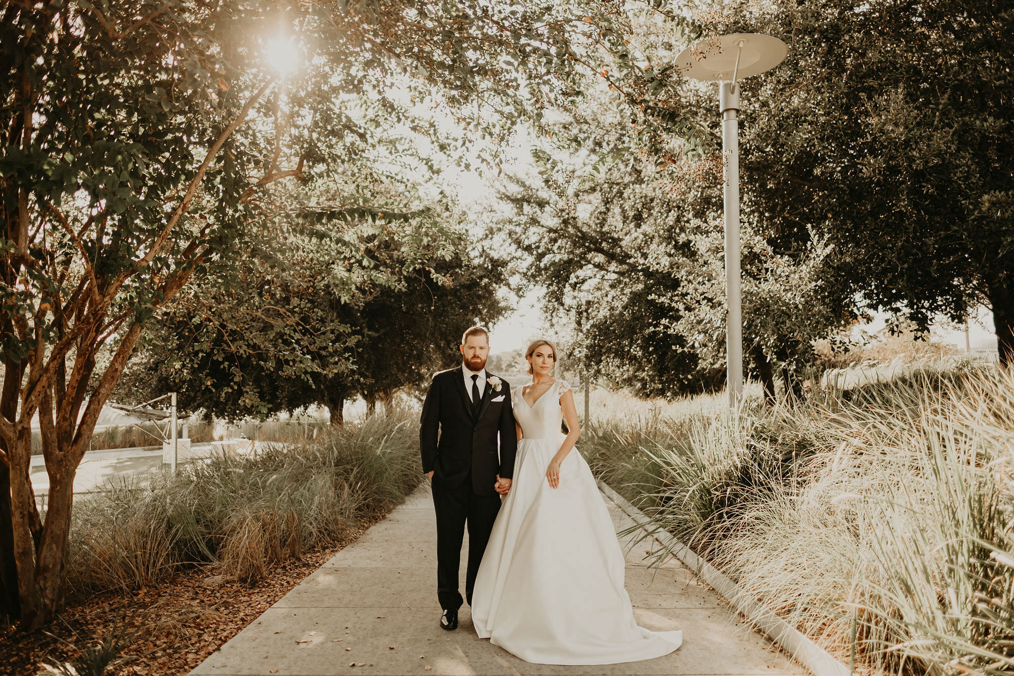 Outdoor Bride and Groom Portrait with Tree Lined Sidewalk | V Neck Low Back Mikado Satin and Lace Ballgown Wedding Dress by Anomalie | Groom wearing Classic Black Suit Tux