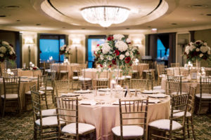 Indoor Wedding Reception at Downtown Tampa Wedding Venue The Tampa Club | Round Reception Tables with Champagne Gold Linen Tablecloths and Gold Chiavari Chairs and Gold Charger Plates | Tall Wedding Centerpieces with White Hydrangea and Red Roses and Eucalyptus Greenery with Cylinder Vase Floating Candles